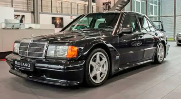Czarny Mercedes 190 Evo z charakterystycznym spojlerem i felgami, stojący w salonie samochodowym.