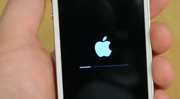 Dłoń trzyma iPhone'a z logo Apple i paskiem postępu, wskazującym na proces hard reset iPhone.