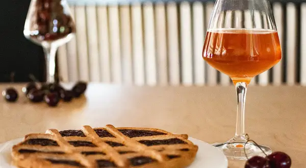 Torta con marmellata di ciliegie e un bicchiere di birra alla ciliegia, con ciliegie fresche sparse sul tavolo.