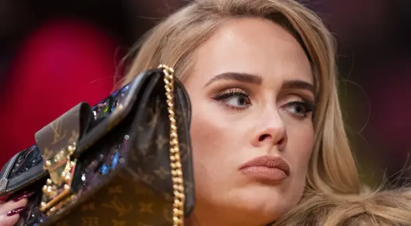 Adele z torebką na koncercie, zamyślona, z makijażem i blond włosami.