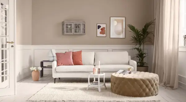 Beige ist die Farbe der Wände, des Sofas und des runden Hockers. Ein gemütliches Wohnzimmer mit weißen Dielen und einem Teppich.