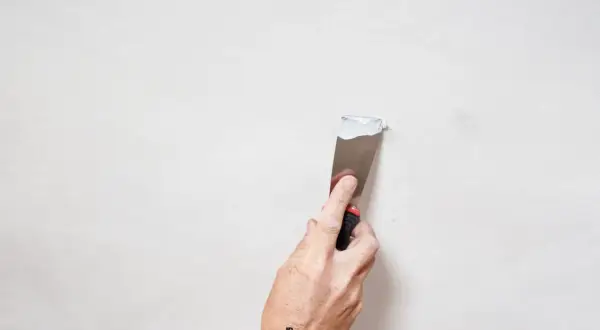 Mano con spatola applica stucco bianco su parete, un passo per come pitturare di bianco una parete gialla.