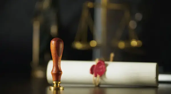 Pieczęć i zwój z czerwonym woskiem, symbolizujące formalności prawne, takie jak wniosek o stwierdzenie nabycia spadku. W tle waga sprawiedliwości.