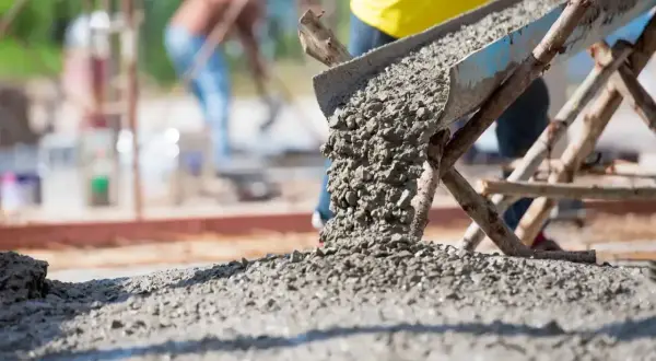 Beton wylewany z rynny na placu budowy. W tle pracownicy. Kluczowe pytanie: ile cementu na kubik betonu?