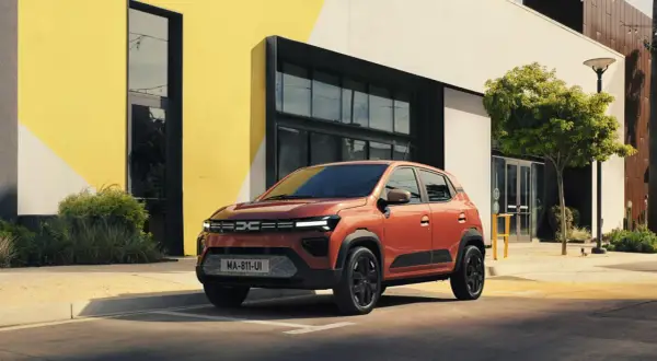 Pomarańczowa Dacia Spring na tle nowoczesnego budynku. Sprawdź atrakcyjną dacia spring cena i wybierz swój wymarzony samochód elektryczny.
