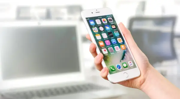 Dłoń trzyma iPhone'a z ikonami aplikacji. Dowiedz się, jak włączyć lokalizację w przeglądarce iPhone, aby korzystać z map i innych funkcji.