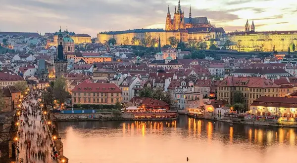 Prague en ce moment : le pont Charles animé, le château illuminé et la Vltava reflétant les lumières de la ville.