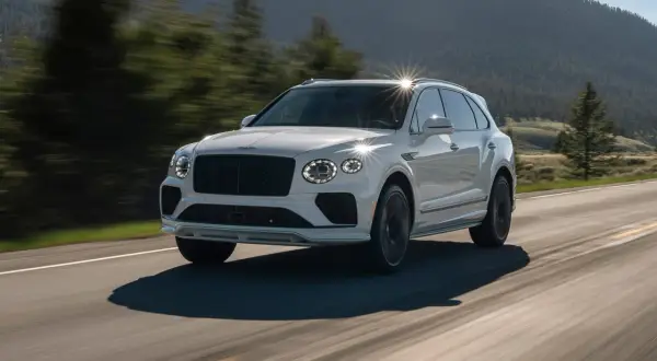 Biały Bentley SUV pędzi po krętej drodze wśród zielonych wzgórz.