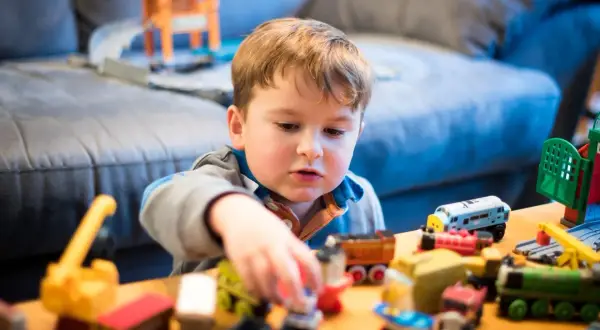 Bambino concentrato nel suo gioco del far finta con tanti trenini e costruzioni colorate.
