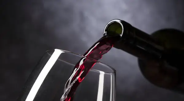 Ciemnoczerwone wino, być może najdroższe wino, leje się z butelki do kieliszka.