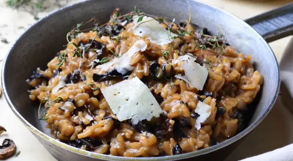Aksamitne risotto z grzybami, udekorowane płatkami parmezanu i gałązkami tymianku, podane w metalowej patelni.