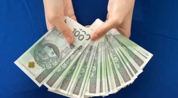 Ręce trzymają stos banknotów 100 zł. Zastanawiasz się, ile dać na 50 urodziny? Taka kwota to dobry początek!