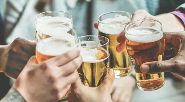 Brindisi con birra, un piacere che, si dice, la birra fa ingrassare. Mani che sollevano bicchieri dorati con schiuma bianca.