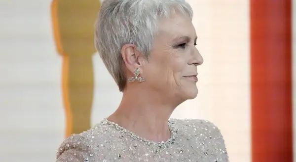 Elegancka kobieta po 50-tce z cieniowanymi, odmładzającymi fryzurami, w błyszczącej sukni i ozdobnych kolczykach.
