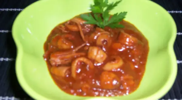 Calamares a la riojana en un plato verde brillante, cubiertos de una salsa roja y decorados con perejil.