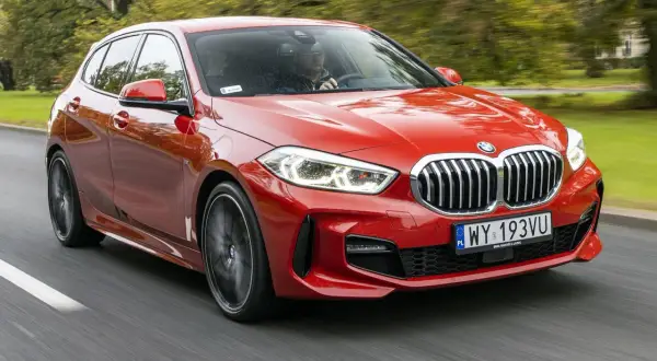 Czerwone BMW F40 pędzi po drodze, otoczone zielenią drzew.