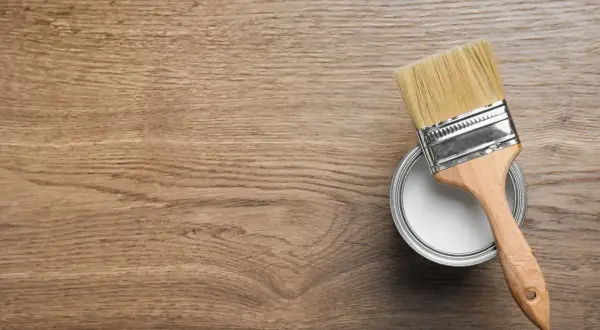 Pennello e barattolo di vernice bianca pronti per colorare legno su una superficie di legno grezzo.