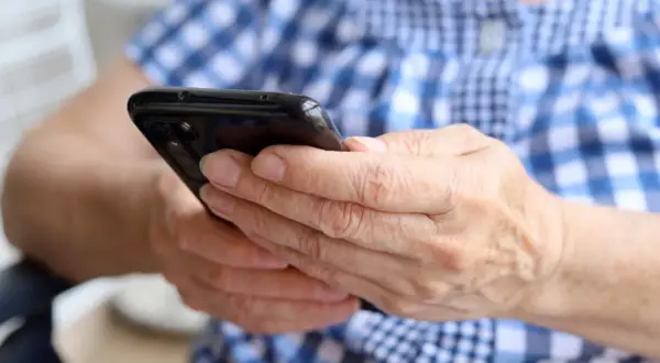Dłonie trzymają czarny smartfon. Zastanawiasz się, jak namierzyć wyłączony telefon?