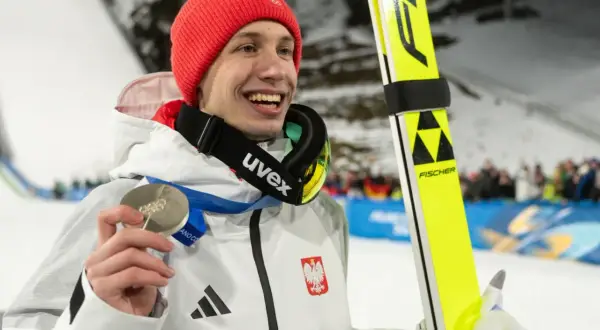 Uśmiechnięty skoczek narciarski w czerwonej czapce trzyma srebrny medal. Czy za dwa medale olimpijskie są dwie emerytury?