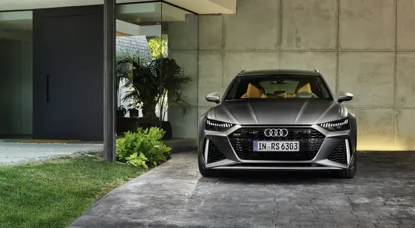 Szary Audi RS6 Avant z beżowym wnętrzem zaparkowany przed nowoczesnym domem. Sprawdź audi rs6 cena.