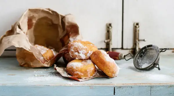 Pączki posypane cukrem pudrem, częściowo w papierowej torbie. Wskazówki, jak przechowywać pączki, by były świeże.