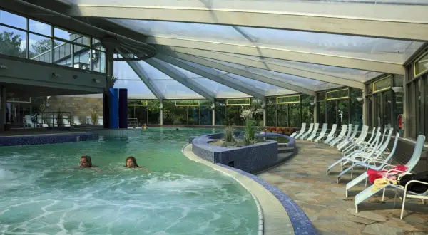 Entspannen in der Therme NRW: Zwei Frauen schwimmen im warmen Wasser unter einem Glasdach, Liegen laden zum Verweilen ein.