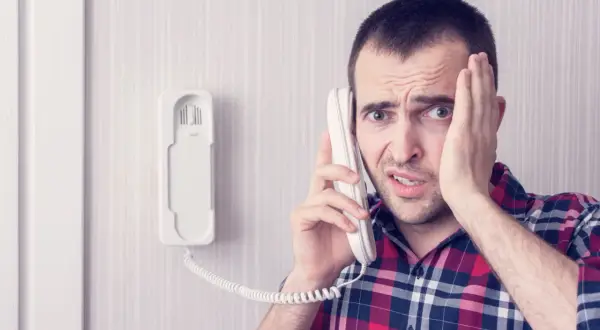 Zmartwiony mężczyzna dzwoni z telefonu domofonowego. Gdzie zgłosić niedziałający domofon?