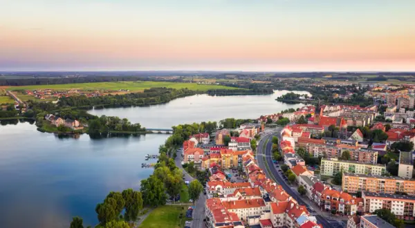 Widok na miasto w krainie wielkich jezior o zachodzie słońca. Domy z czerwonymi dachami, jezioro i zieleń.