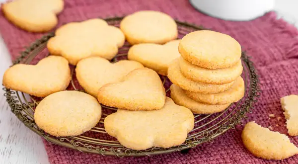 Deliziosi dolci da fare in casa, biscotti a forma di cuore e fiori su un cestino di metallo, pronti per essere gustati.