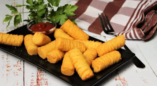 Goldbraune Kroketten, frisch zubereitet, liegen auf einem schwarzen Teller. Dazu gibt es Ketchup und frische Petersilie. Perfekt zum selber machen!
