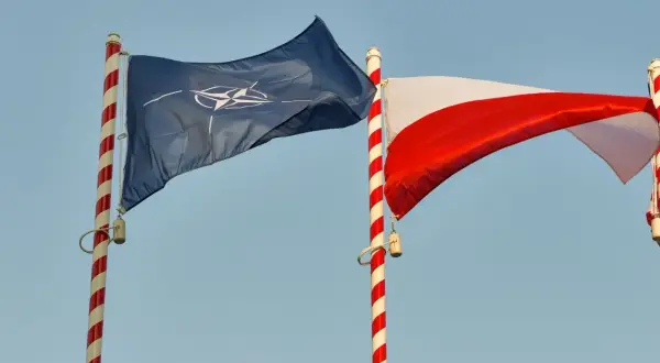 Flaga NATO i biało-czerwona flaga Polski powiewają na tle błękitnego nieba. Dwa państwa NATO razem.