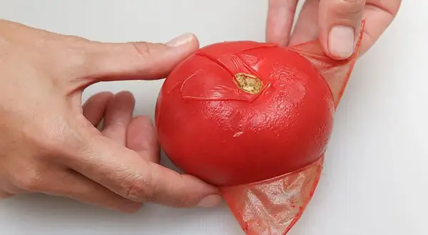 Manos pelando un tomate rojo, mostrando cómo quitar la piel fácilmente.