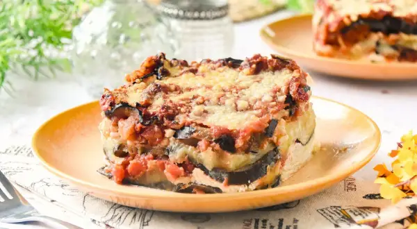 Porción de lasaña de berenjena horneada, con capas de berenjena, salsa de tomate y queso derretido, servida en un plato naranja.
