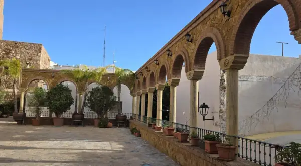 Un patio con arcos de piedra y columnas, palmeras y plantas en macetas. Un lugar encantador que ver en Vera, con un cielo azul despejado.