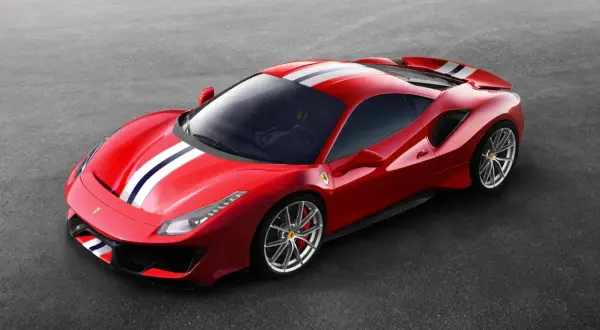 Czerwone Ferrari Pista z białymi i niebieskimi pasami na masce i dachu, zaparkowane na szarym asfalcie.