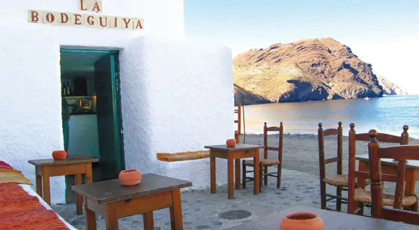 Mesas y sillas de madera en la terraza de "La Bodeguilla", con vistas al mar y a las barcas las negras.