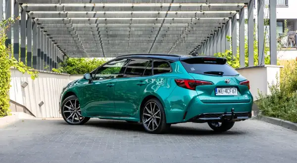 Zielona Toyota Corolla Hybrid kombi z czarnym dachem, zaparkowana pod nowoczesną pergolą.