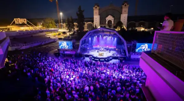 Ein belebtes **Prag Festival** mit einer großen Menge, die einer Band auf einer beleuchteten Bühne zusieht.