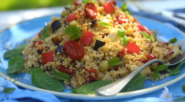 Piatto colorato di cous cous integrale con verdure miste, pomodorini e basilico. Un'idea gustosa per le tue cous cous integrale ricette.