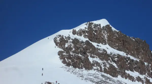 Grupa alpinistów wspina się na najwyższy szczyt Grenlandii, pokonując śnieżne zbocza i skaliste fragmenty.