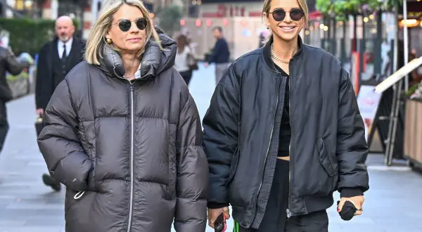 Dwie kobiety w okularach przeciwsłonecznych spacerują ulicą, prezentując copenhagen style w obszernych kurtkach puchowych i bomberkach.