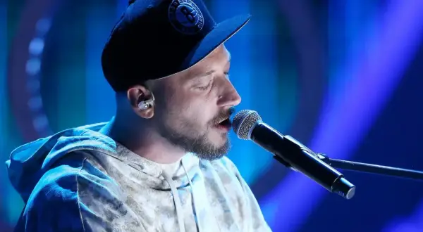 Artysta w czapce z daszkiem śpiewa do mikrofonu. W jego oczach widać emocje, jakby opowiadał historię: "kortezy co w tobie i we mnie".