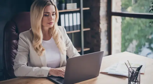 Kobieta w jasnej marynarce pracuje nad odpowiedzią na pozew przy laptopie w biurze.