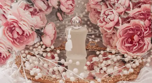 Flakonik Valaya Parfums de Marly otoczony różowymi różami i perłami, na złotym lustrzanym tacy.