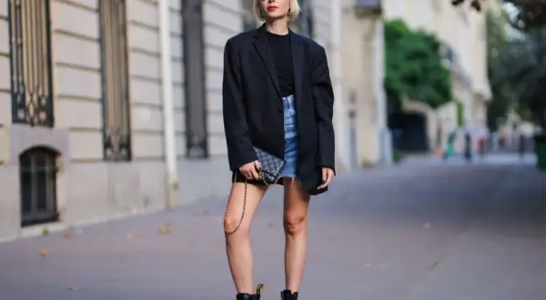 Kobieta w czarnym blazerze i jeansowej spódniczce nosi kultowe buty Dr. Martens, które mają bogatą historię.