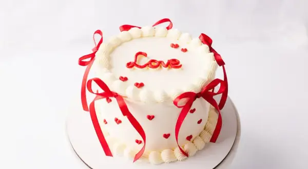 Uroczy tort bento ozdobiony czerwonymi serduszkami i wstążkami, z napisem "Love" na wierzchu. Idealny na Walentynki.