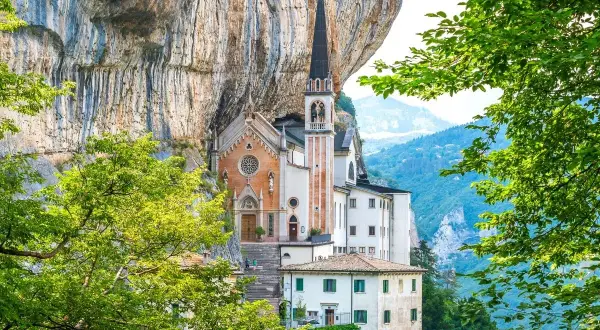 Suggestiva chiesa incastonata nella roccia, un gioiello architettonico vicino al Lago di Garda, circondata da verde lussureggiante e montagne.