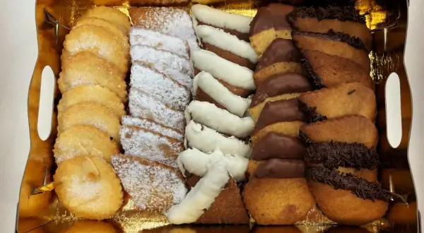 Bandeja dorada con surtido de galletas: almendradas, espolvoreadas con azúcar glas, bañadas en chocolate blanco y negro. ¡La mejor pastelería Zaragoza!