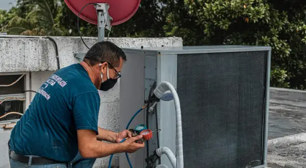 Technik sprawdza czujnik ciśnienia klimatyzacji, podłączając manometr do jednostki zewnętrznej.
