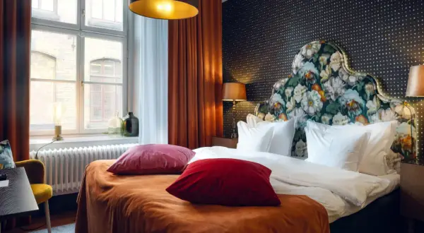 Ett lyxigt rum på nofo hotell Stockholm med en stor säng, blommig huvudgavel och orangea sammetsgardiner.